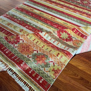May include: A rectangular area rug with a striped pattern in shades of red, yellow, orange, and green. The rug features a geometric design and fringe along the edges. The rug is placed on a wooden floor.