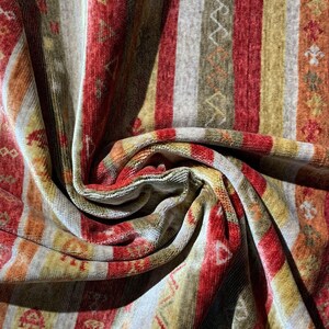 May include: Close-up of a patterned fabric with vertical stripes in shades of red, gold, orange, and gray. The fabric has a soft, textured appearance with geometric and floral designs.