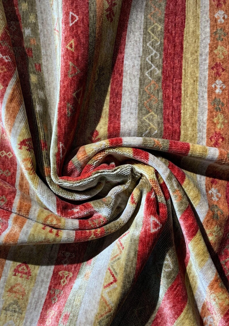 May include: Close-up of a patterned fabric with vertical stripes in shades of red, gold, orange, and gray. The fabric has a soft, textured appearance with geometric and floral designs.