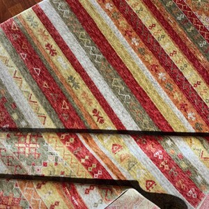 May include: A colorful area rug with a striped pattern in shades of red, yellow, green, and gray. The rug features geometric designs and is partially rolled up, revealing the underside.