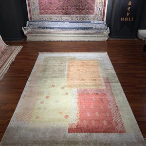 May include: A rectangular area rug with a muted color palette. The rug features a light beige background with sections of peach, orange, and red. The design includes geometric shapes and patterns. The rug has a fringe along the bottom edge.