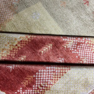 May include: Close-up of a patterned textile with a mix of colors. The design features geometric shapes and arrow-like motifs in shades of red, yellow, and beige. The fabric appears to be folded, revealing layers of the pattern.