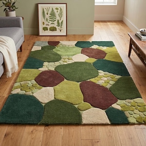 Puede incluir: Una alfombra rectangular con un patrón de piedra en tonos verdes, marrones y crema. La alfombra presenta grandes parches de color de forma irregular, creando un diseño natural y orgánico. La alfombra está colocada sobre un suelo de madera.