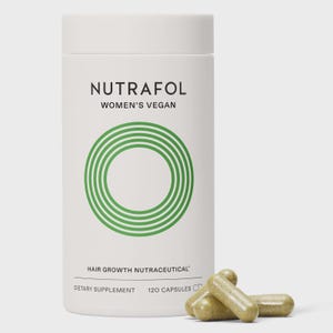 May include: A white cylindrical bottle of Nutrafol Women's Vegan hair growth nutraceutical dietary supplement. The bottle has a green circular design and the text "Nutrafol" in black. 120 capsules are included. Several capsules are in front of the bottle.