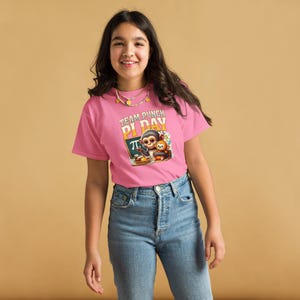 May include: A pink t-shirt with the text "TEAM PUNCH PI DAY" and a graphic of a monkey, a pie, and the Pi symbol. The shirt is worn by a person wearing blue jeans.