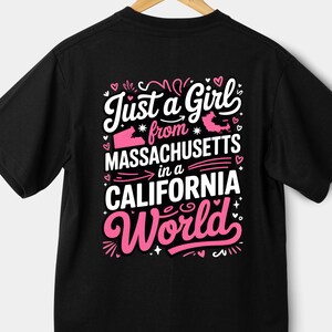 Peut inclure: T-shirt noir avec un motif graphique rose et blanc. Le texte dit "Juste une fille du Massachusetts dans un monde californien". Le motif comprend les formes du Massachusetts et de la Californie, avec des cœurs et des étoiles.