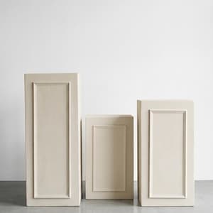 May include: Three rectangular display pedestals in a matte cream finish. Each pedestal features a raised rectangular frame molding on the front face. The set consists of two taller pedestals flanking a shorter central pedestal, all with flat tops.
