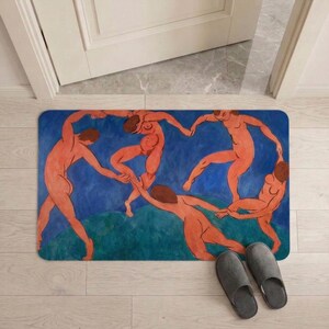 May include: Rectangular doormat featuring a painting of nude figures dancing in a circle against a blue and green background. The artwork is a vibrant display of human forms in motion. Gray slippers are placed near the mat.