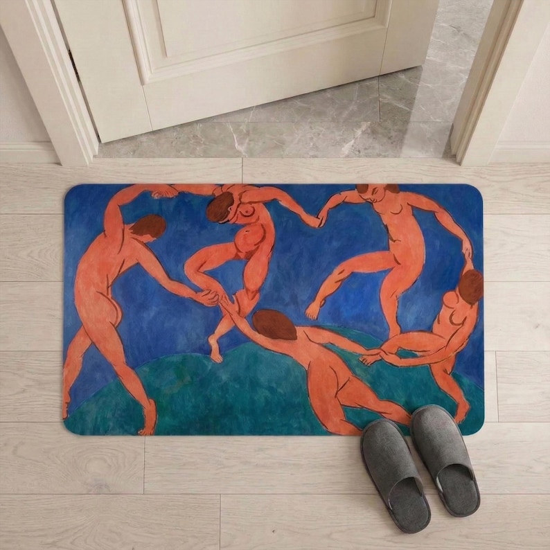 May include: Rectangular doormat featuring a painting of nude figures dancing in a circle against a blue and green background. The artwork is a vibrant display of human forms in motion. Gray slippers are placed near the mat.