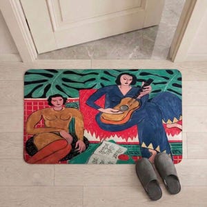 May include: Rectangular doormat featuring a colorful illustration of two women, one playing a guitar. The design includes a green background with large leaf shapes, red accents, and musical notes. Gray slippers are placed near the mat.