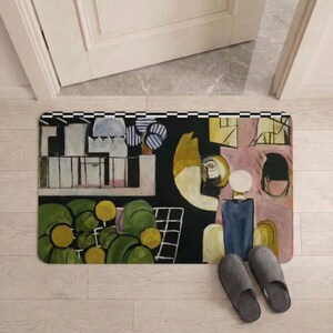 May include: Rectangular doormat with an abstract art design in shades of green, yellow, black, and pink. The mat features a black and white checkered border and is placed in front of a white door. Gray slippers are next to the mat.