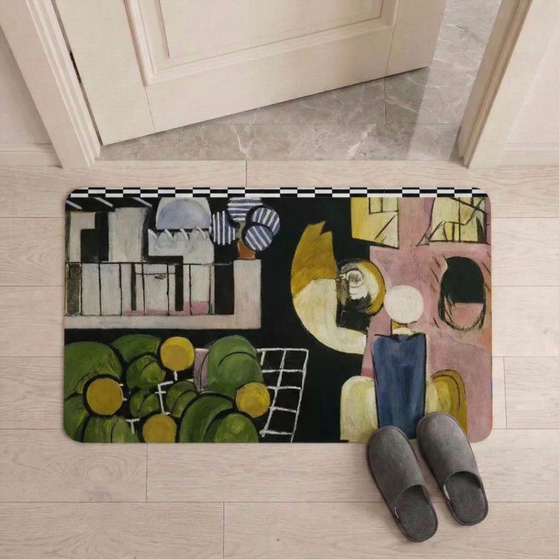 May include: Rectangular doormat with an abstract art design in shades of green, yellow, black, and pink. The mat features a black and white checkered border and is placed in front of a white door. Gray slippers are next to the mat.