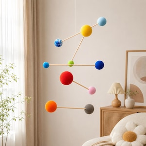 May include: A hanging mobile featuring multiple spheres in various colors including yellow, red, orange, blue, pink, green, and grey, connected by thin wooden rods. One blue sphere has a white marbled pattern, while the others are solid colors.
