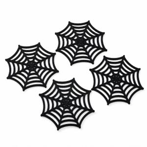 May include: A set of four black coasters, each featuring a die-cut spider web design. The coasters are shaped like octagonal webs with radiating lines and concentric circles, providing a flat surface for drinks while maintaining a distinct spider web pattern.