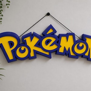 May include: A blue and yellow "Pokémon" logo sign hanging on a white wall. The sign is made of layered material, with a blue outline and yellow interior. A black string is used for hanging.
