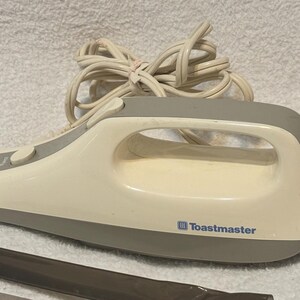 Puede incluir: Cuchillo el&eacute;ctrico para trinchar crema y gris con mango y cable. El cuchillo tiene una base y un mango grises, con la marca "Toastmaster" impresa en el lateral. Se ven dos cuchillas.