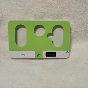 Könnte beinhalten: Ein hellgrünes und weißes elektronisches Gerät mit digitaler Anzeige und mehreren Tasten. Das Gerät hat eine einzigartige Form mit Aussparungen und dem Text "ySky". Ein farbenfrohes Schmetterlingslogo ist ebenfalls sichtbar.
