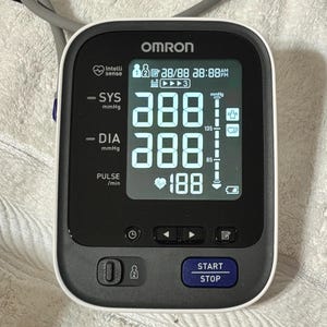 May include: An Omron blood pressure monitor with a digital screen displaying SYS and DIA readings of 288 mmHg, a pulse of 188 beats per minute, and a battery icon. The device features a dark gray control panel with a blue START STOP button.