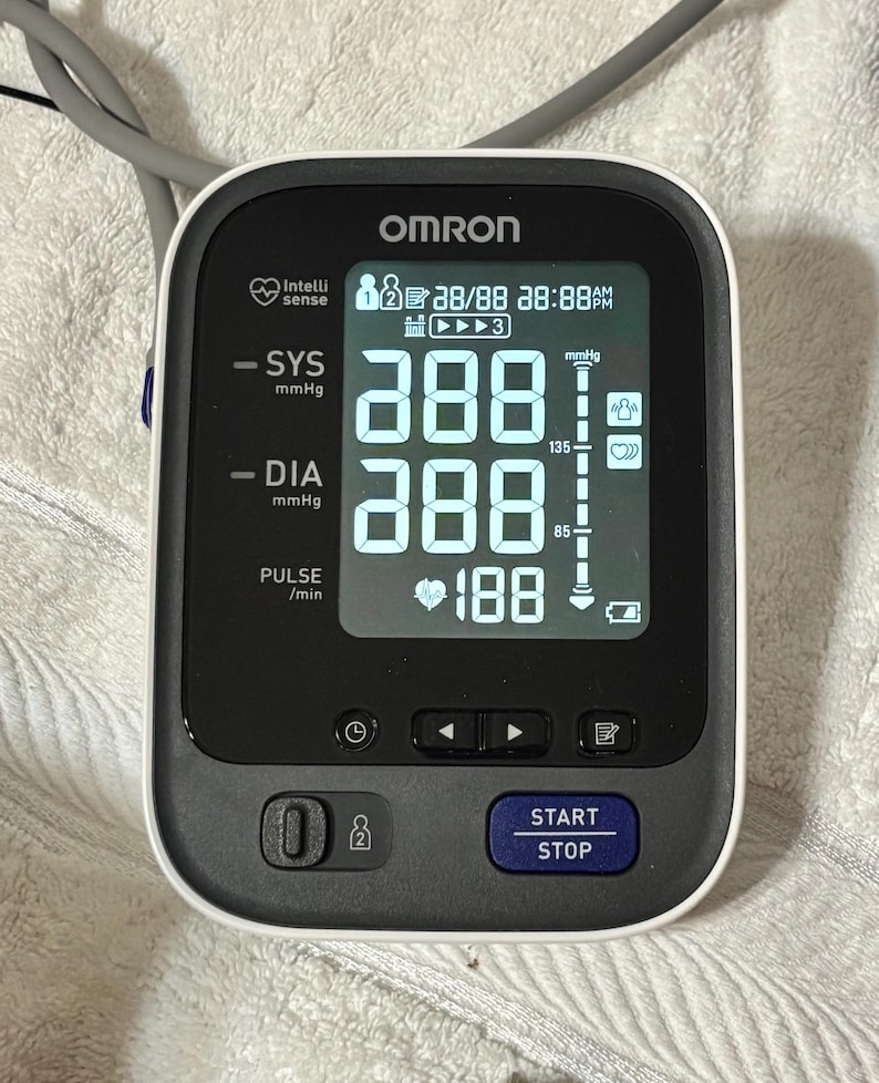 May include: An Omron blood pressure monitor with a digital screen displaying SYS and DIA readings of 288 mmHg, a pulse of 188 beats per minute, and a battery icon. The device features a dark gray control panel with a blue START STOP button.