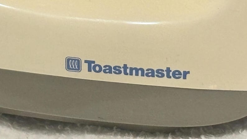 Puede incluir: Primer plano de un electrodom&eacute;stico color crema con el texto azul "Toastmaster". El nombre de la marca se muestra de forma destacada en la parte frontal del electrodom&eacute;stico. El electrodom&eacute;stico tiene una forma redondeada.
