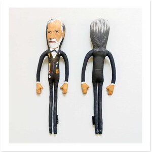 May include: Two fabric dolls, one facing forward and one facing backward, both dressed in black suits. The front-facing doll has a detailed face with a white beard and hair, and a bow tie. The doll has long arms and legs, and tan hands and feet.