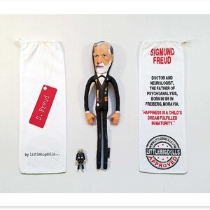 May include: A fabric doll of Sigmund Freud in a black suit, white shirt, and bow tie, with a miniature figurine and two white drawstring bags. One bag has a red tag that reads "S. Freud". The other bag has text about Freud.