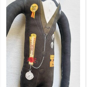 May include: A fabric doll dressed in a black suit with a white shirt and bow tie. The doll has a pocket watch attached to a chain and a scroll that reads "FONDEMENT DE LA PSYCHANALYSE". A gold badge reads "Goethe Preis 1940".