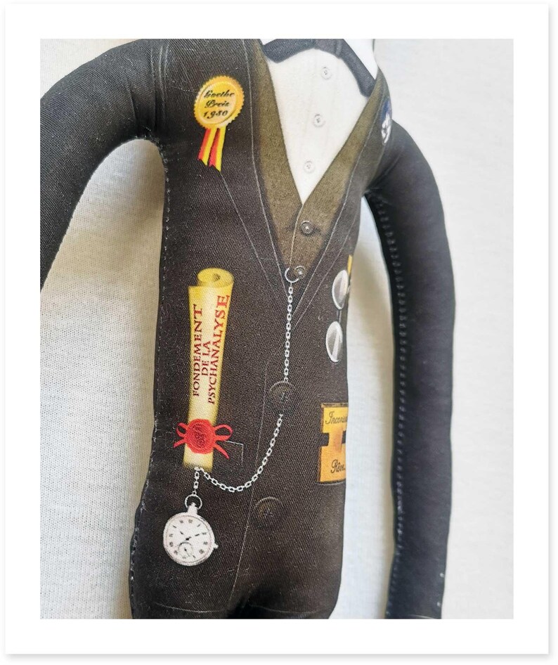 May include: A fabric doll dressed in a black suit with a white shirt and bow tie. The doll has a pocket watch attached to a chain and a scroll that reads "FONDEMENT DE LA PSYCHANALYSE". A gold badge reads "Goethe Preis 1940".