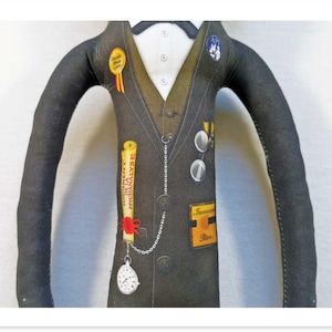 May include: A stuffed doll dressed in a dark gray suit with a white shirt and bow tie. The doll has a pocket watch, a scroll, and several pins and badges. The scroll reads "FONDEMENT DE LA PSYCHANALYSE".