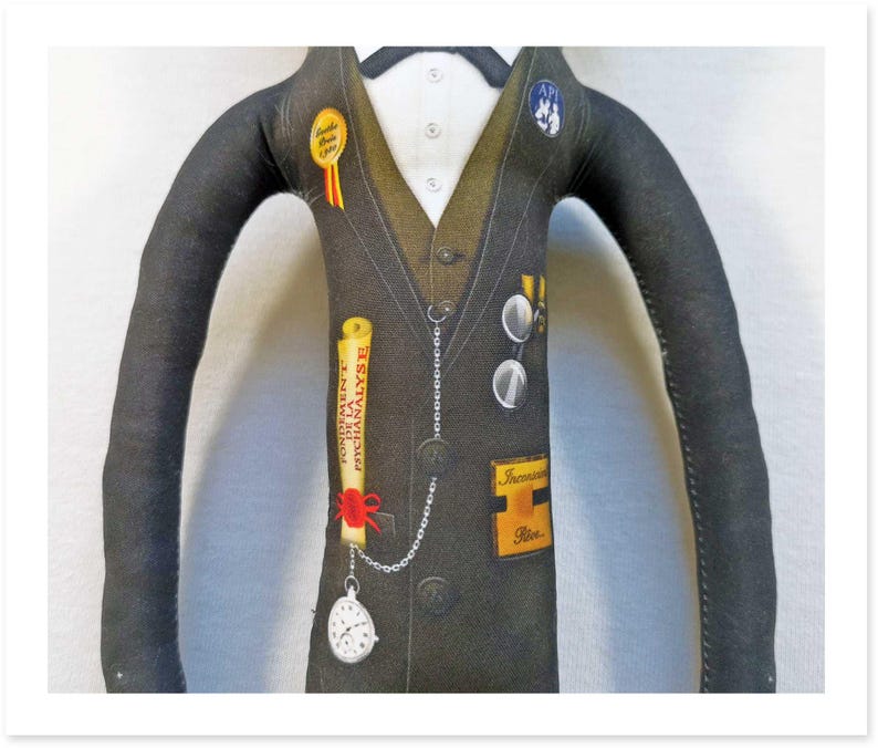 May include: A stuffed doll dressed in a dark gray suit with a white shirt and bow tie. The doll has a pocket watch, a scroll, and several pins and badges. The scroll reads "FONDEMENT DE LA PSYCHANALYSE".