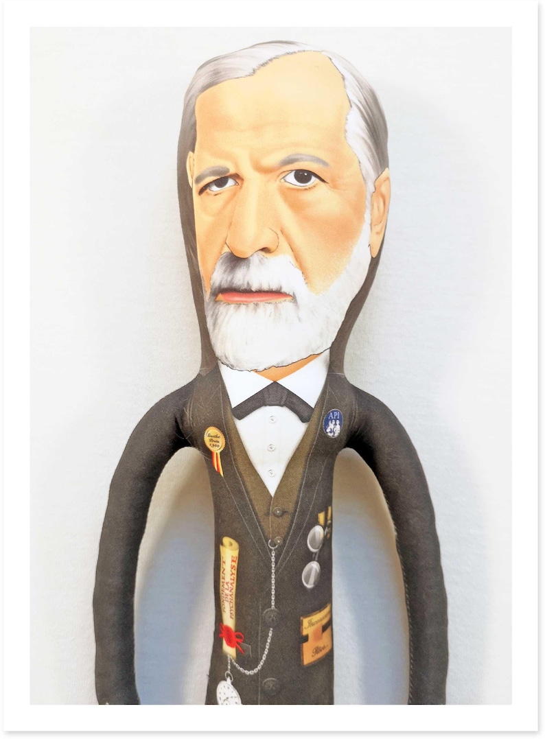 May include: A fabric doll depicting a distinguished man with a white beard and hair, wearing a dark suit with a bow tie. The doll has several pins and a scroll with text. The doll's face is painted with realistic features.