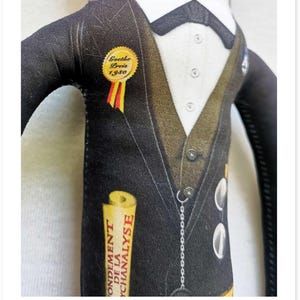 May include: A fabric doll dressed in a black suit with a white shirt and bow tie. The doll has a gold Goethe Preis 1930 pin and a scroll that reads "Fondement de la Psychanalyse."