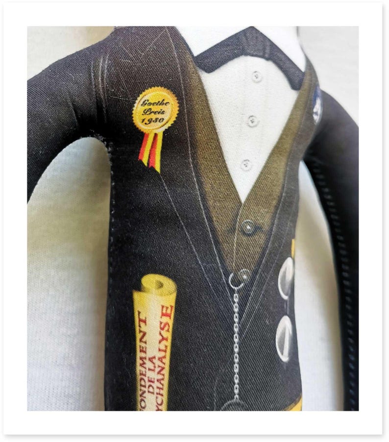 May include: A fabric doll dressed in a black suit with a white shirt and bow tie. The doll has a gold Goethe Preis 1930 pin and a scroll that reads "Fondement de la Psychanalyse."
