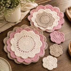 Op de afbeelding: Een verzameling handgemaakte gehaakte doilies en onderzetters in verschillende maten en tinten roze, beige en wit. De doilies hebben een geschulpte rand en een ingewikkeld openwerkontwerp, perfect voor woondecoratie.