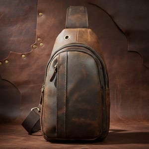 Könnte beinhalten: Braune Leder-Umhängetasche mit Used-Look. Die Tasche hat ein Hauptfach mit Reißverschluss, eine kleinere Vordertasche und einen verstellbaren Schultergurt. Die Tasche ist aus reichhaltigem, dunkelbraunem Leder.