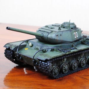 Op de afbeelding: Een schaalmodel van een groene militaire tank met een lang op de koepel gemonteerd kanon, zwarte rupsbanden en het nummer 20 in het wit op de zijkant van de koepel geschilderd. Het model bevat gedetailleerde wielen en een verweerde afwerking.