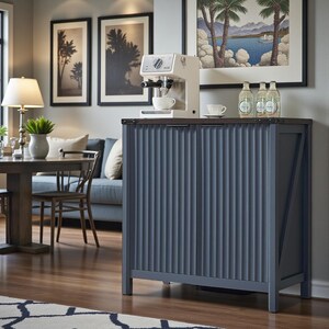 May include: A blue cabinet with vertical ribbed detailing and a dark wood top. A white espresso machine sits on top, with a cup underneath. Two bottles and a framed picture are also on the cabinet. The cabinet is in a room with a dining table and artwork.