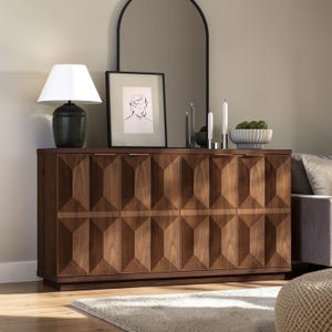 May include: A dark brown wooden sideboard with geometric door panels. The sideboard is topped with a lamp, artwork, candles, and a decorative bowl. A black arched mirror is mounted on the wall behind the sideboard.