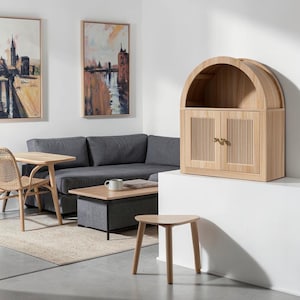 May include: A light wood cabinet featuring an arched top and two doors with vertical fluted detailing. The cabinet has small, round brass-toned knobs and an open storage shelf located directly beneath the arched upper section of the unit.