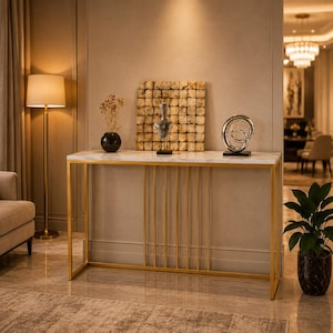 May include: A rectangular console table featuring a white marble top and a gold-finished metal frame with vertical bar accents. The table is positioned against a wall and holds a black vase with dried flowers, a sculpture, and a silver spiral object.