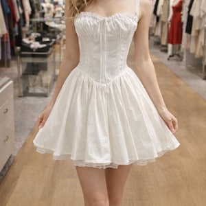 May include: A white dress with a corset-style bodice and a flared skirt. The dress features delicate lace trim along the neckline and hem. The dress has spaghetti straps and a tie detail at the bust.