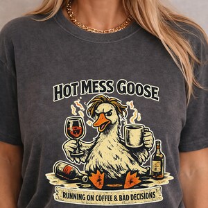 May include: Dark gray t-shirt with a graphic of an angry goose holding a wine glass and coffee mug. Text reads "HOT MESS GOOSE" above the goose and "RUNNING ON COFFEE & BAD DECISIONS" below.