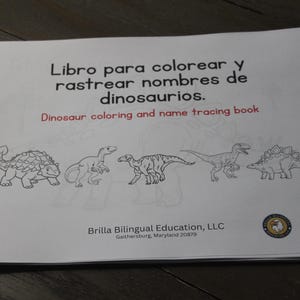 Puede incluir: Un libro blanco titulado "Dinosaur coloring and name tracing book" en ingl&eacute;s y espa&ntilde;ol. La portada presenta dibujos lineales negros de cinco dinosaurios. Publicado por Brilla Bilingual Education, LLC.