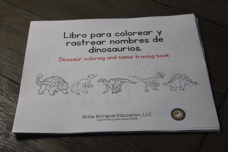 Puede incluir: Un libro blanco titulado "Dinosaur coloring and name tracing book" en ingl&eacute;s y espa&ntilde;ol. La portada presenta dibujos lineales negros de cinco dinosaurios. Publicado por Brilla Bilingual Education, LLC.