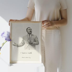 Peut inclure: Un portrait encadré en noir et blanc de Martin Luther King Jr. L'œuvre présente une illustration détaillée de King en costume, avec le texte "I have a mate" et son nom en dessous. Le cadre est en bois clair.
