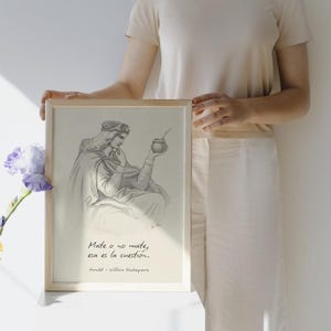 Puede incluir: Un boceto a lápiz enmarcado representa una figura sosteniendo una taza de mate, con el texto "Mate o no mate, esa es la cuestión." debajo. La obra de arte está en un marco de madera clara.