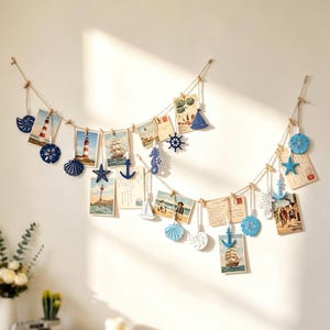 Puede incluir: Una decoración de pared con temática náutica que consiste en una cuerda de yute con pequeñas pinzas de madera que sujetan postales y fotografías, intercaladas con figuras de madera en azul y blanco de anclas, conchas y barcos.