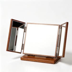 May include: A tri-fold vanity mirror featuring a central rectangular glass panel flanked by two smaller, adjustable side panels. The frame and the rectangular base are constructed from dark brown wood, with visible silver metal hinges.