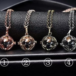May include: Four pendant necklaces with round, openwork cages and dark centers are displayed. The necklaces are in rose gold, gold, and silver tones, each with a matching chain. The pendants are numbered 1 through 4.