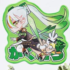 Op de afbeelding: Een groene patch met een anime-stijl karakter met wit haar en groene accenten, die een prei-achtig wapen vasthoudt. Een cartoonvogel met een strenge uitdrukking is ook aanwezig. Japanse tekst staat onderaan.